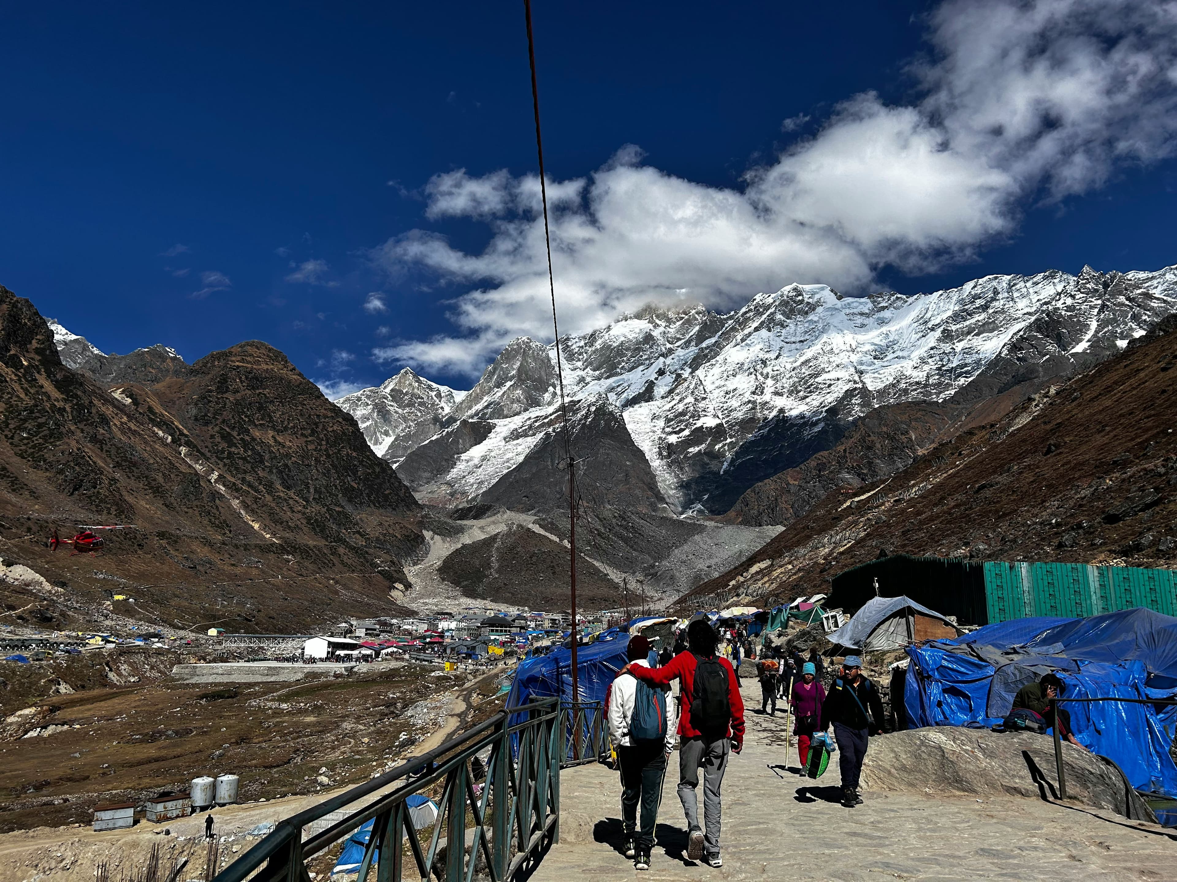 Trekkers walking towards Kedarnath with snow-covered Himalayan peaks in the background at 3,583m altitude