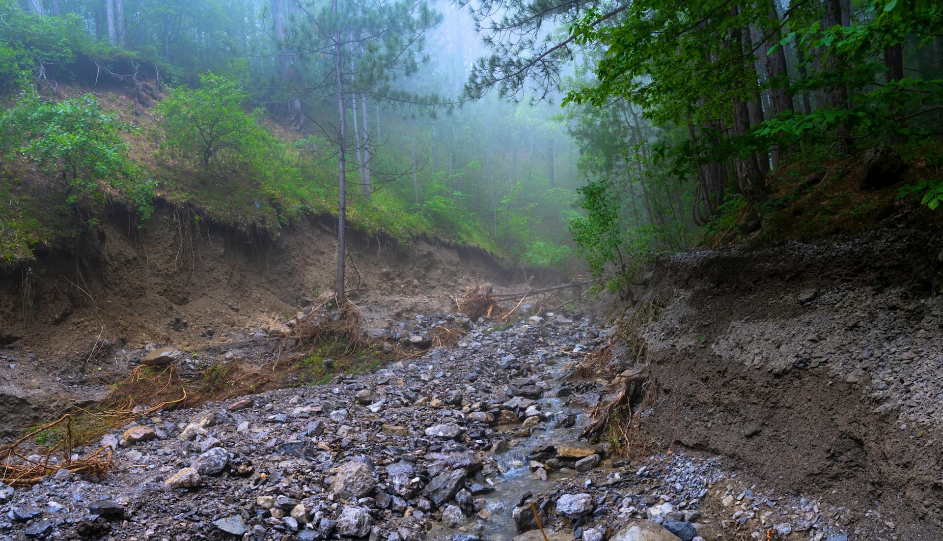 Landslide debris and erosion on a mountain road during monsoon season with mist and rain
