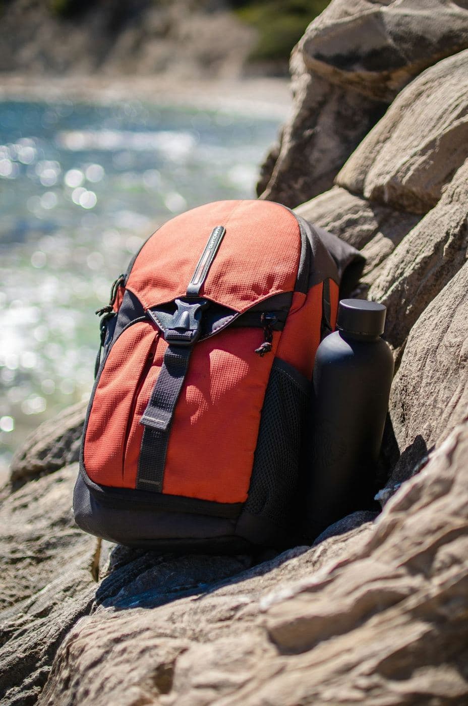 Orange daypack with water bottle resting on rocks near a mountain stream