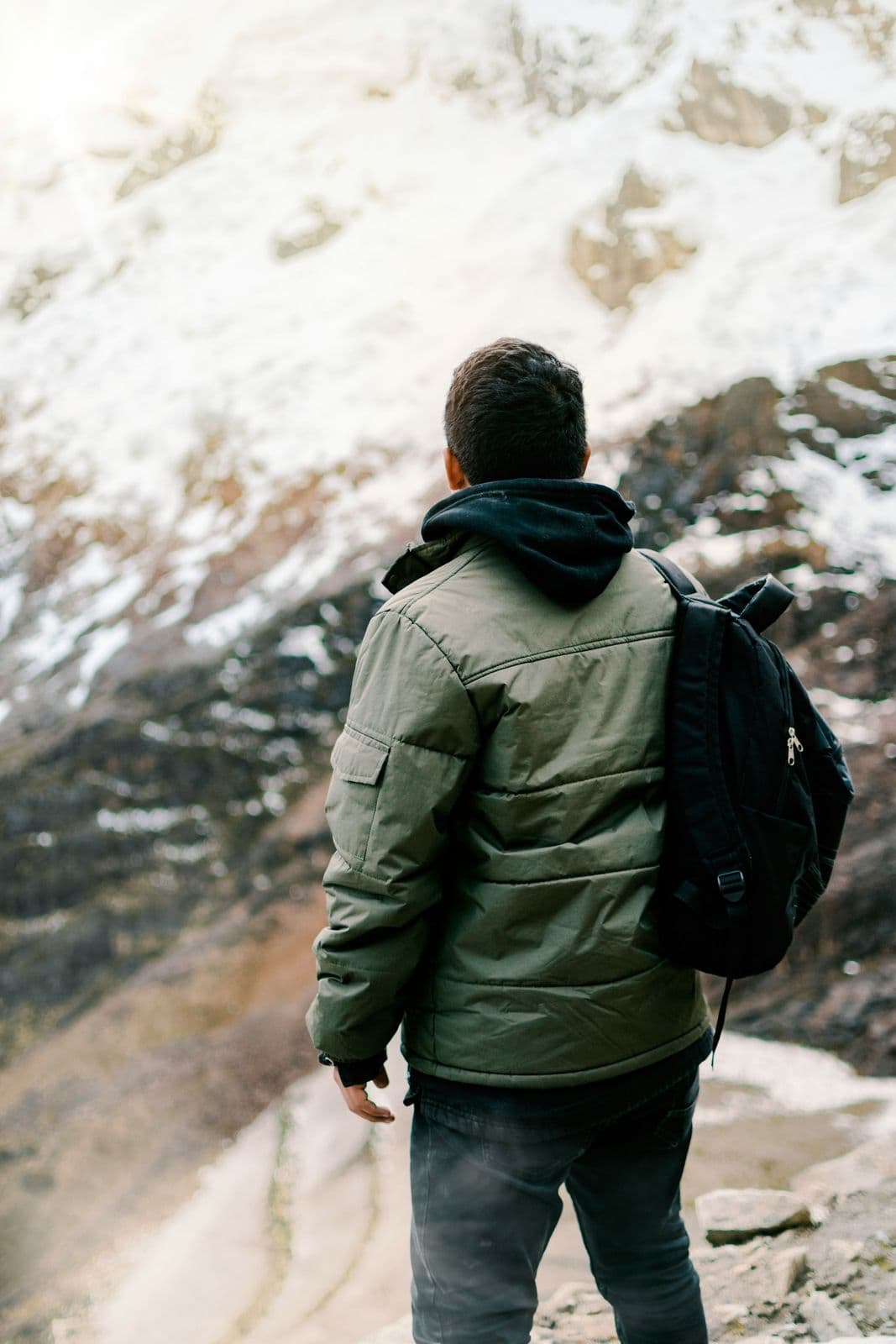 Trekker in layered jacket with backpack facing snow-covered Himalayan peaks