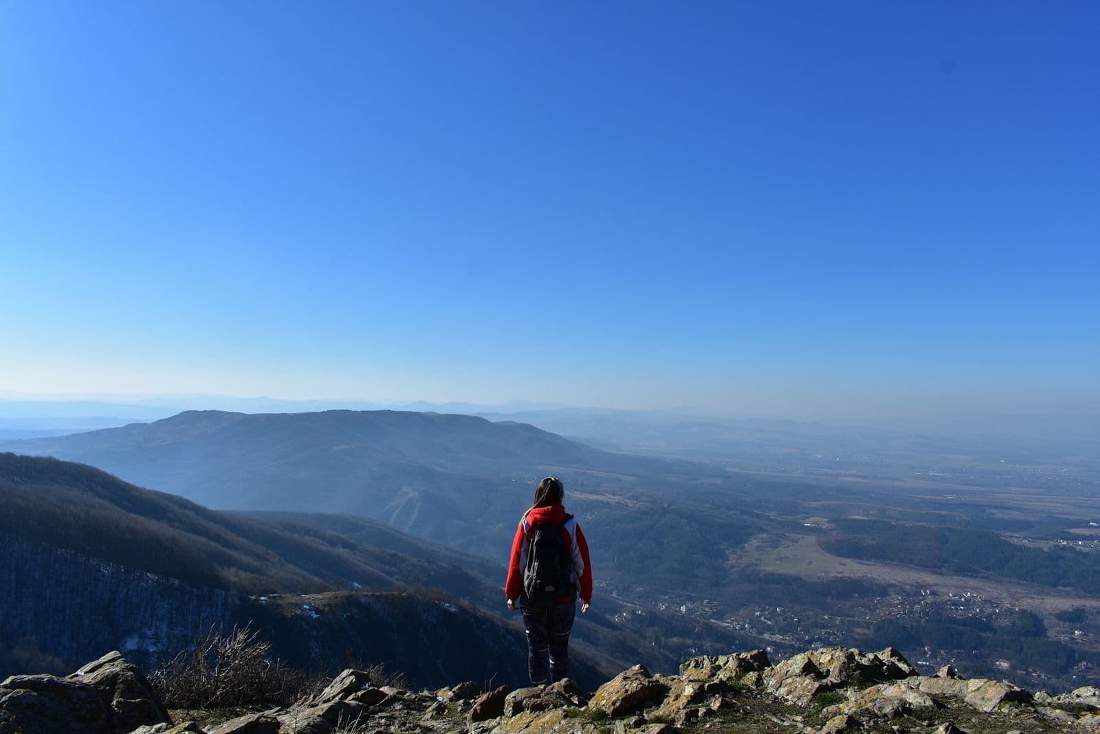Trekker in red jacket standing on mountain summit overlooking vast valley