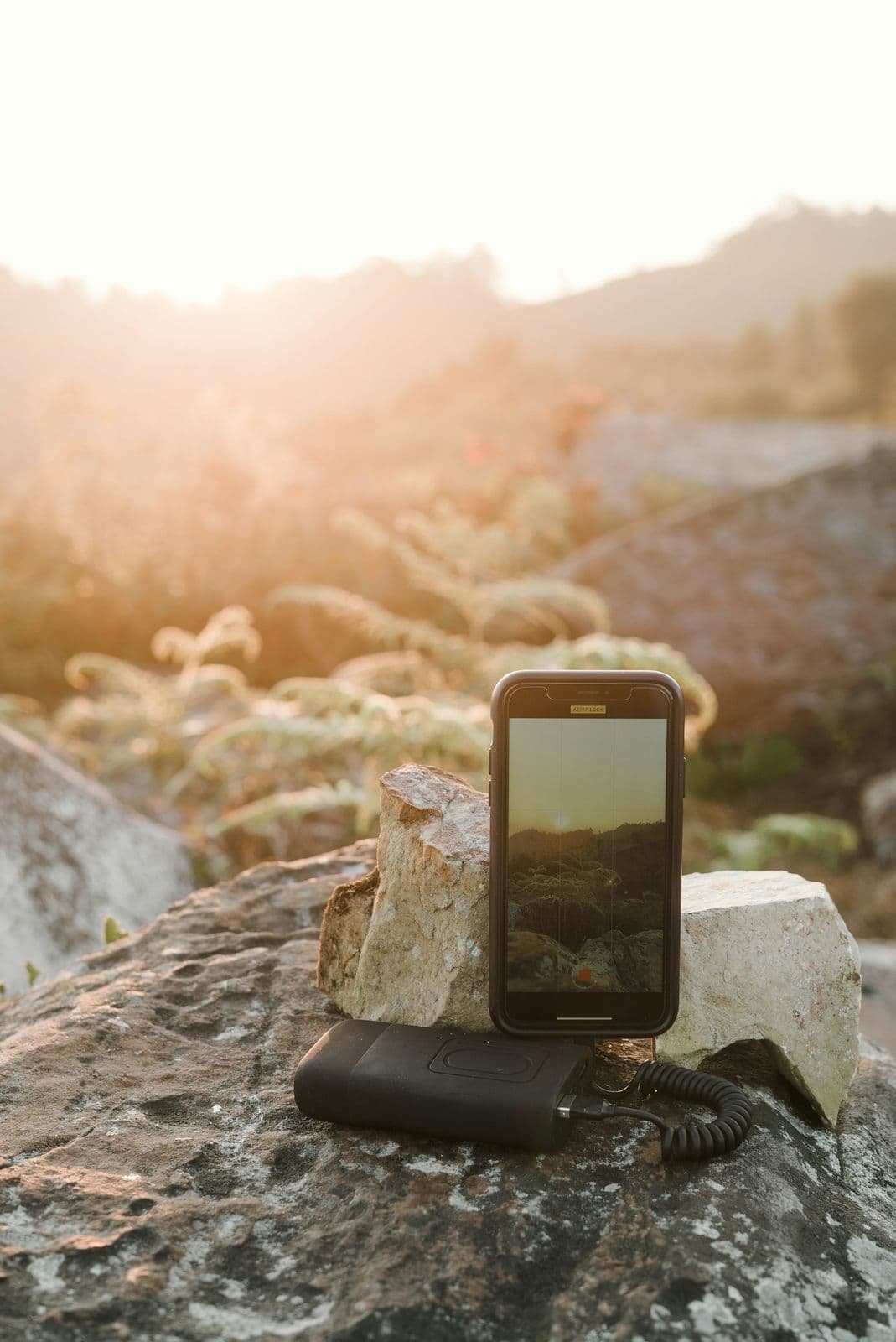 Power bank charging smartphone on a rock at sunset during a mountain trek