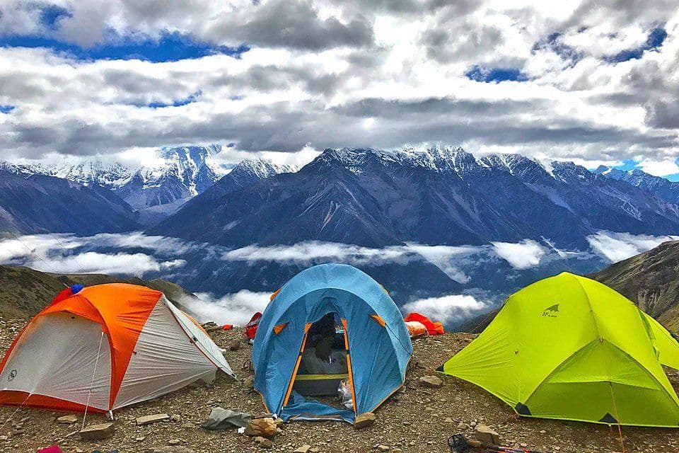 Colorful camping tents at high altitude with snow-capped Himalayan peaks and clouds
