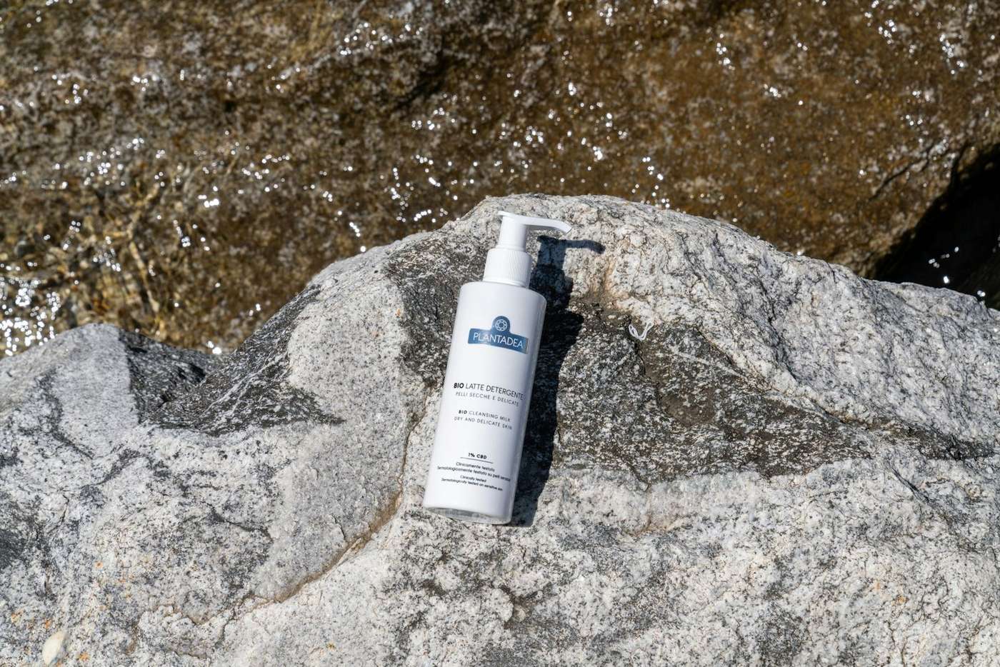 Sunscreen bottle on a mountain rock with water glistening in the background