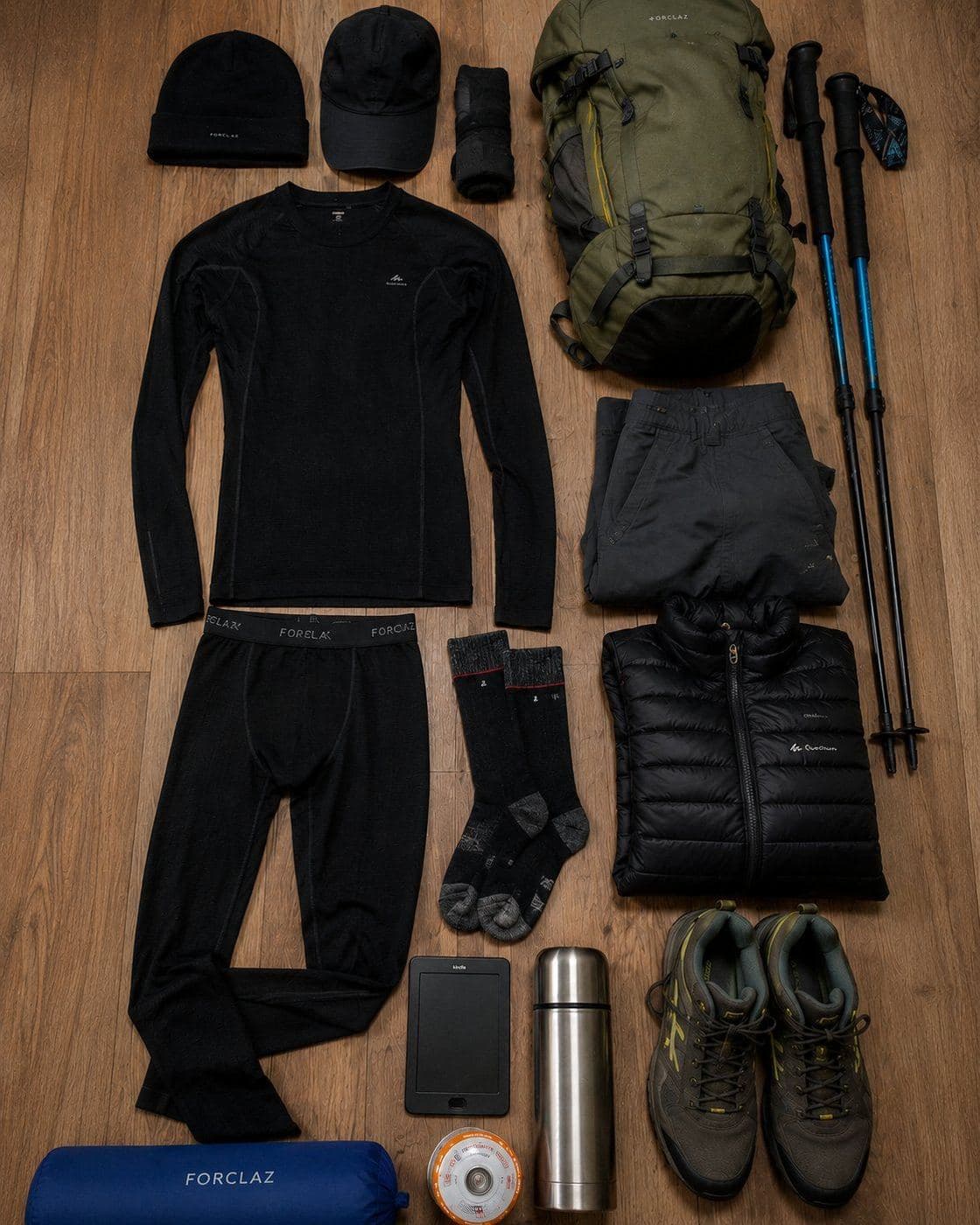 Trekking thermal base layers and gear laid out flat with backpack boots and down jacket