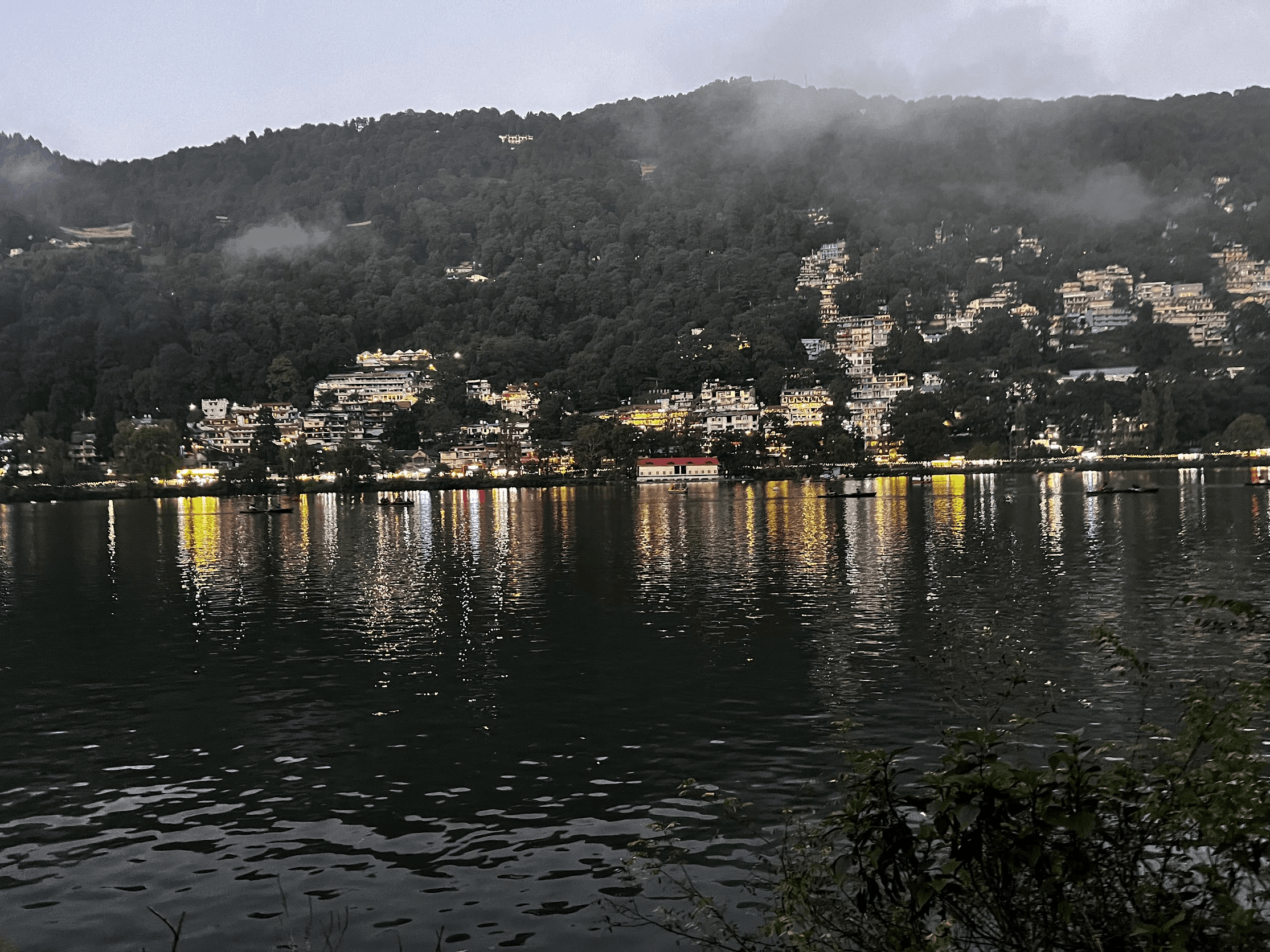 Naini Lake after sunset with town lights reflected in the water and low clouds over the hillside