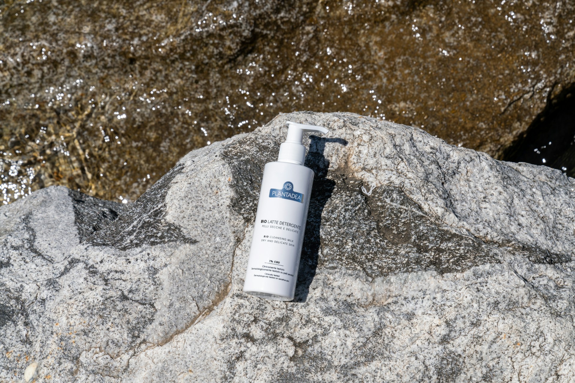 Sunscreen bottle on a mountain rock with water glistening in the background
