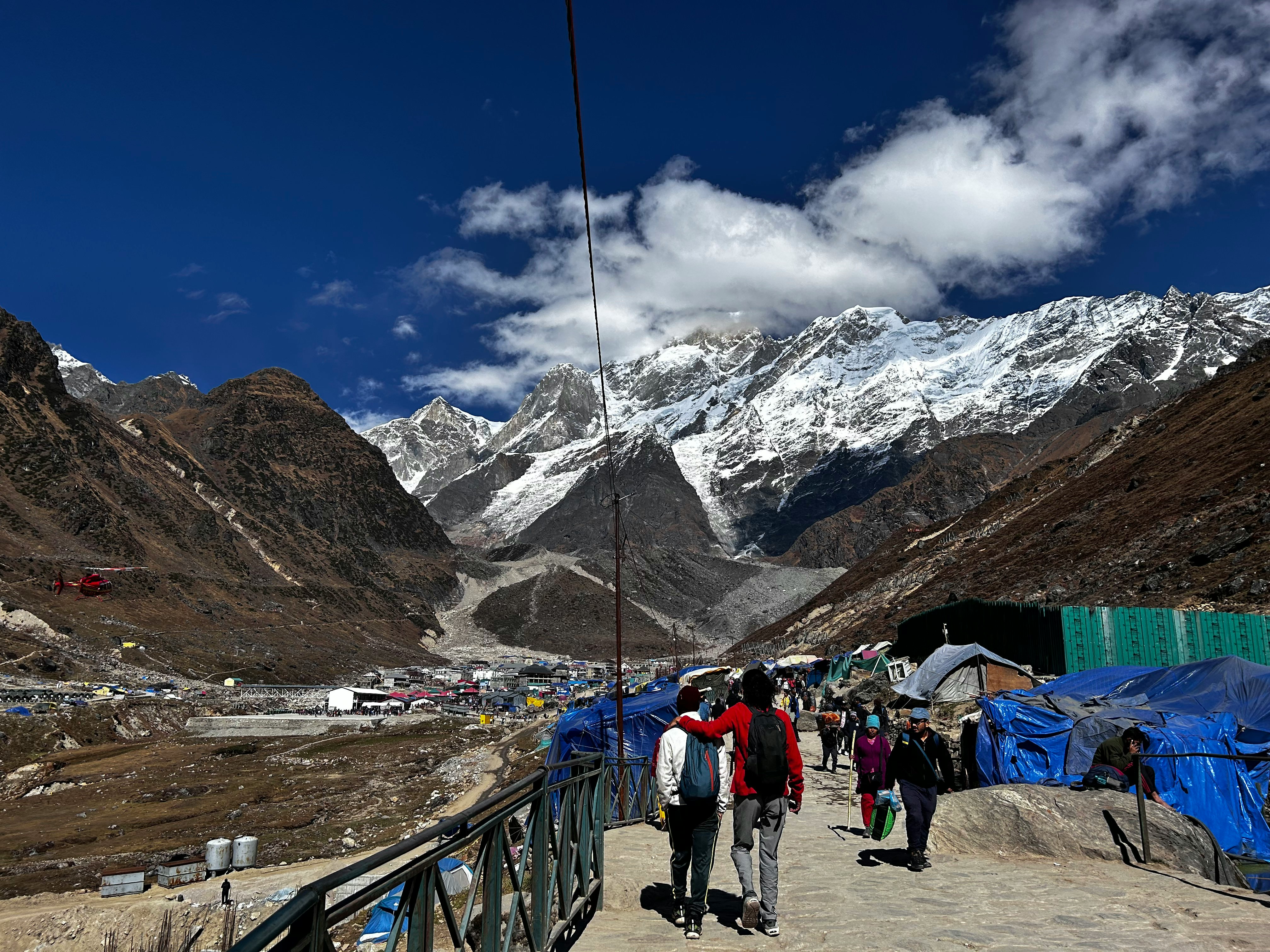 Trekkers walking towards Kedarnath with snow-covered Himalayan peaks in the background at 3,583m altitude