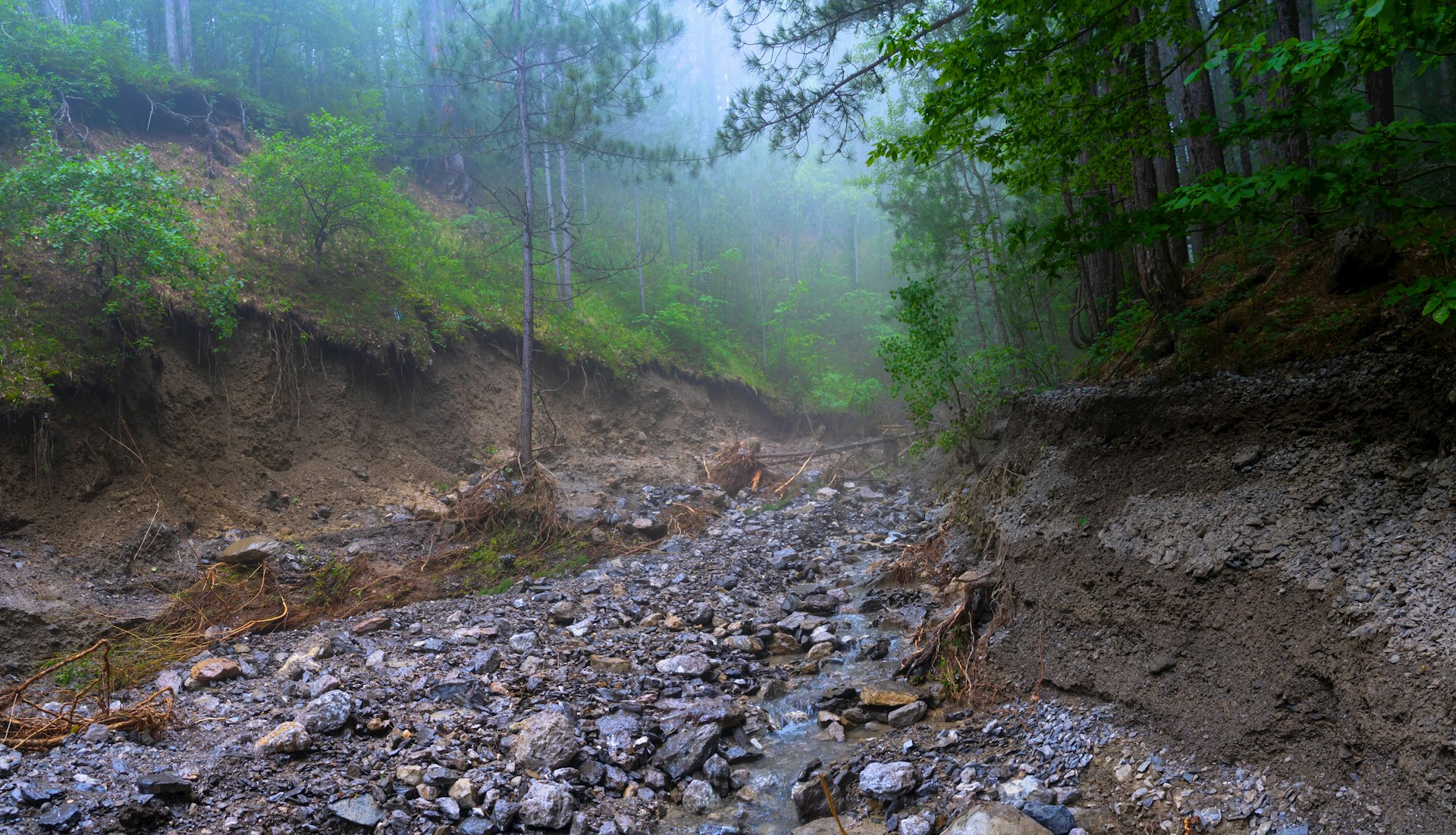 Landslide debris and erosion on a mountain road during monsoon season with mist and rain